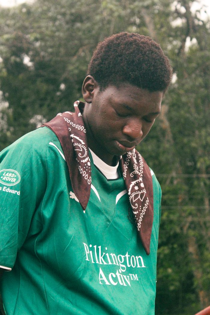 services-03 A young male soccer player wearing a green jersey stands outdoors, looking thoughtful.