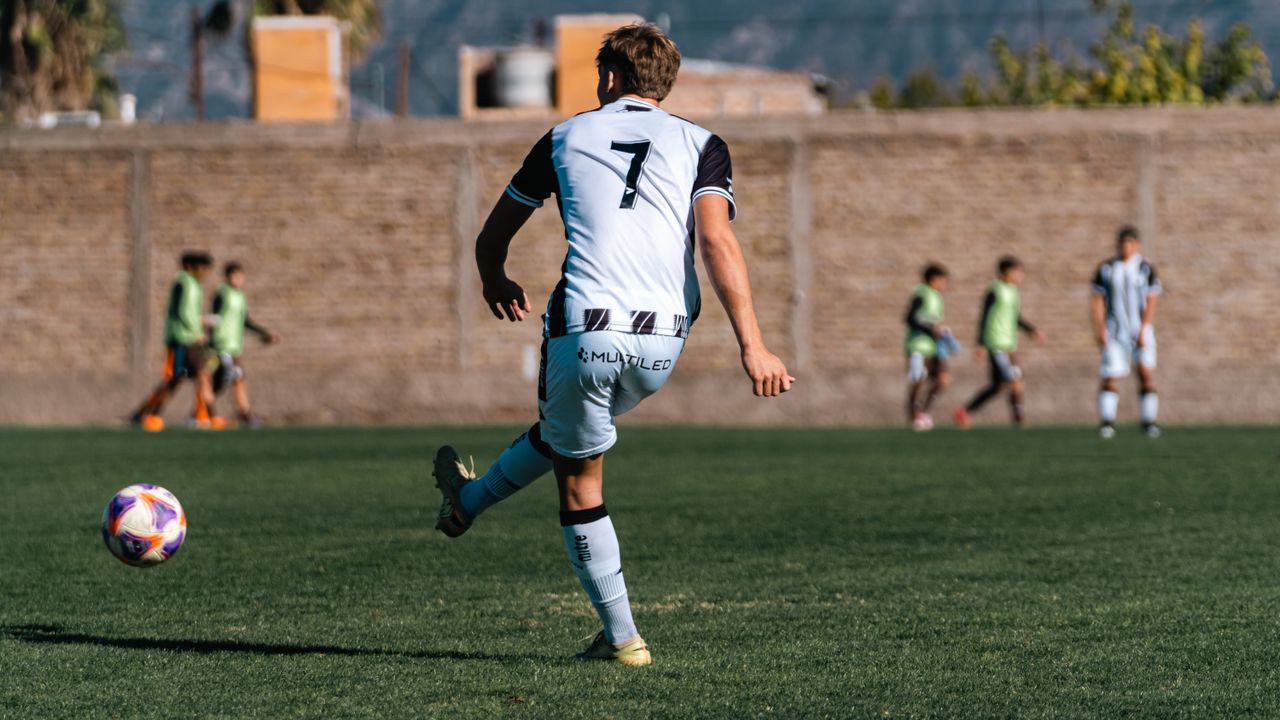 Soccer player in action on field during daytime match with teammates in background.
